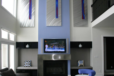 他の地域にあるおしゃれなリビング (青い壁、カーペット敷き、標準型暖炉、金属の暖炉まわり、壁掛け型テレビ) の写真