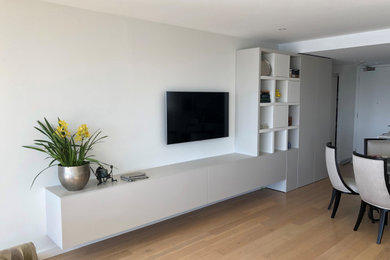 Ejemplo de salón para visitas abierto moderno de tamaño medio con paredes blancas, suelo laminado y televisor colgado en la pared