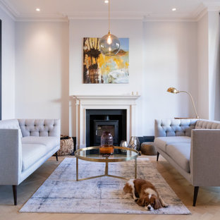 Inspiration for a medium sized contemporary open plan living room in London with a reading nook, white walls, light hardwood flooring, a standard fireplace, a plastered fireplace surround and beige floors.
