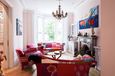Foto på ett eklektiskt separat vardagsrum, med ett finrum, rosa väggar, mellanmörkt trägolv, en standard öppen spis och en spiselkrans i trä