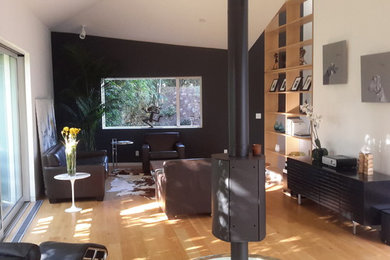 Foto de salón para visitas abierto moderno de tamaño medio sin televisor con paredes negras, suelo de madera clara, chimeneas suspendidas y marco de chimenea de metal