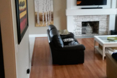 Medium tone wood floor living room photo in Vancouver with beige walls, a standard fireplace, a wood fireplace surround and a wall-mounted tv