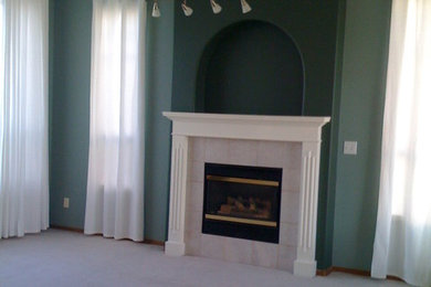 他の地域にある中くらいなおしゃれなリビング (緑の壁、カーペット敷き、標準型暖炉、漆喰の暖炉まわり) の写真