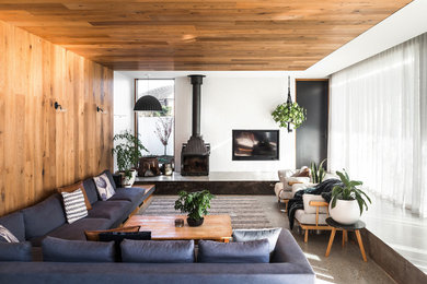 Aménagement d'un grand salon contemporain ouvert avec un mur blanc, sol en béton ciré, un poêle à bois, un sol gris, un manteau de cheminée en béton et un téléviseur dissimulé.