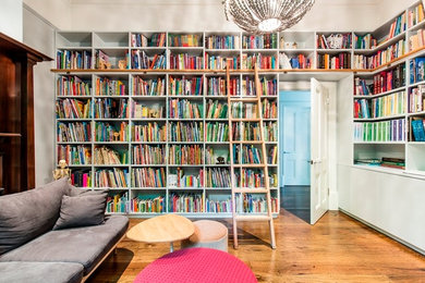 Cette photo montre un grand salon chic avec une bibliothèque ou un coin lecture, un mur gris, un sol en bois brun, une cheminée standard, un manteau de cheminée en bois et aucun téléviseur.