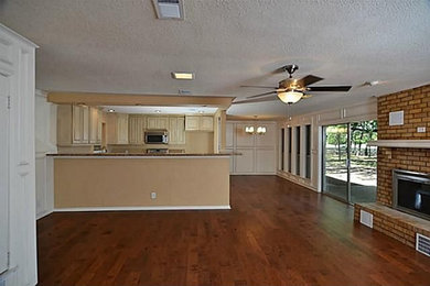 Mittelgroßes, Offenes Klassisches Wohnzimmer mit beiger Wandfarbe, braunem Holzboden, Kamin und Kaminumrandung aus Backstein in Dallas