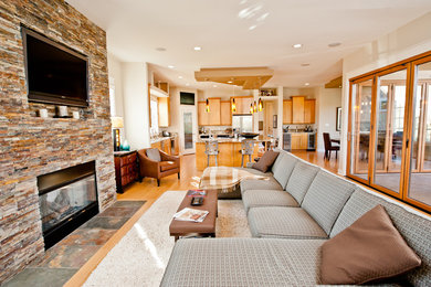 Cette image montre un salon design ouvert avec une cheminée standard, un manteau de cheminée en pierre et un téléviseur fixé au mur.