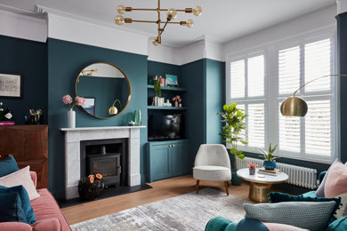 Abgetrenntes, Mittelgroßes Klassisches Wohnzimmer mit grüner Wandfarbe, gefliester Kaminumrandung, freistehendem TV, braunem Boden, braunem Holzboden und Kaminofen in Kent