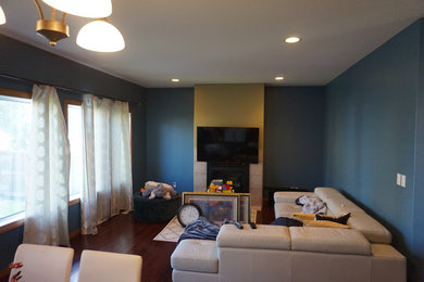 Modelo de salón abierto con suelo de madera en tonos medios, todas las chimeneas, marco de chimenea de baldosas y/o azulejos, televisor colgado en la pared, suelo rojo y paredes azules