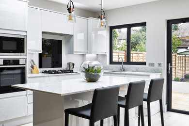 Example of a trendy l-shaped light wood floor and beige floor kitchen design in London with an undermount sink, flat-panel cabinets, white cabinets, stainless steel appliances, an island and white countertops