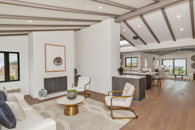 Example of a mid-sized mid-century modern formal and open concept medium tone wood floor, brown floor and exposed beam living room design in San Diego with white walls, a standard fireplace, a plaster fireplace and no tv
