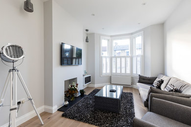 Medium sized contemporary enclosed living room in London with grey walls, a wall mounted tv and brown floors.