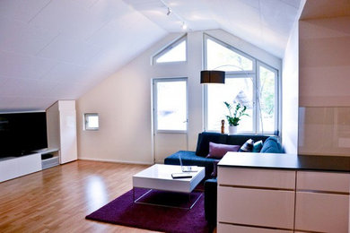 Ejemplo de salón abierto contemporáneo de tamaño medio con paredes blancas, suelo de madera clara y televisor independiente