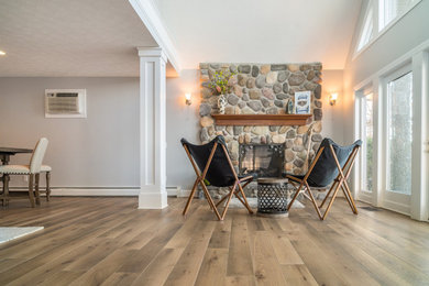 Ejemplo de salón abierto costero grande con paredes grises, suelo de madera clara, marco de chimenea de piedra y suelo marrón