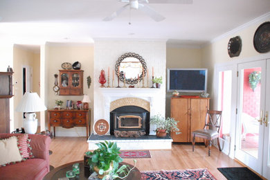 Imagen de salón para visitas clásico de tamaño medio con paredes beige, suelo de madera clara, todas las chimeneas, marco de chimenea de metal y televisor colgado en la pared