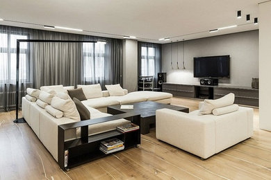 Modelo de salón abierto contemporáneo grande sin chimenea con paredes grises, suelo de madera clara, televisor colgado en la pared y suelo beige