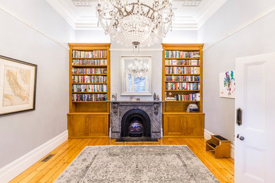 Example of a mid-sized classic medium tone wood floor living room library design in Melbourne with gray walls, a standard fireplace, a stone fireplace and no tv