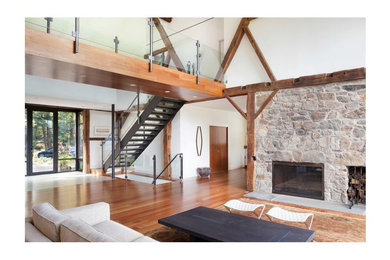 Cette image montre un très grand salon design ouvert avec un mur blanc, un sol en bois brun, une cheminée standard et un manteau de cheminée en pierre.