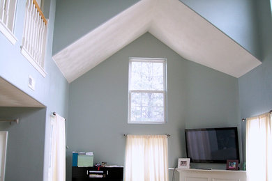Ejemplo de biblioteca en casa abierta de tamaño medio con paredes azules y televisor colgado en la pared