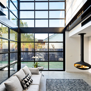Immagine di un soggiorno contemporaneo di medie dimensioni e stile loft con pareti bianche, pavimento in cemento, camino sospeso e TV autoportante