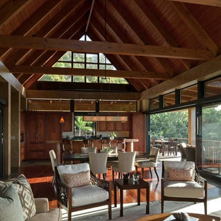 Immagine di un grande soggiorno tropicale aperto con pareti beige, parquet scuro, camino classico, cornice del camino in intonaco, nessuna TV e pavimento marrone