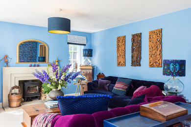 Imagen de salón bohemio grande con paredes azules, moqueta, estufa de leña, marco de chimenea de piedra y papel pintado