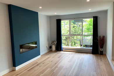 Example of a mid-sized trendy open concept light wood floor and multicolored floor living room design in Vancouver with blue walls, a standard fireplace and a plaster fireplace