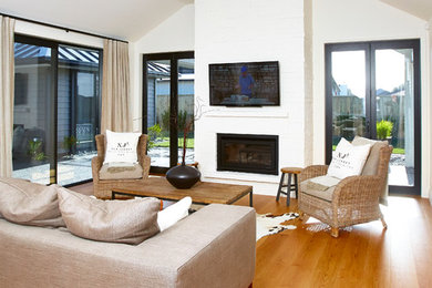 Photo of a medium sized contemporary open plan living room in Hamilton with white walls, medium hardwood flooring, a standard fireplace, a brick fireplace surround and a wall mounted tv.