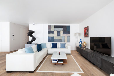 This is an example of a large contemporary formal open plan living room in London with white walls, a freestanding tv, light hardwood flooring and beige floors.
