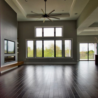 Idee per un grande soggiorno moderno aperto con pareti grigie, parquet scuro, camino lineare Ribbon, cornice del camino in intonaco, TV a parete, pavimento marrone e soffitto ribassato