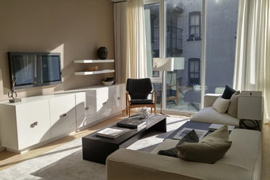 Foto de salón abierto contemporáneo de tamaño medio con paredes beige, suelo de madera clara, televisor colgado en la pared y suelo beige