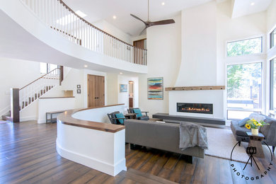 Cette photo montre un grand salon ouvert avec un mur blanc, parquet foncé, une cheminée standard, un manteau de cheminée en plâtre et un sol marron.