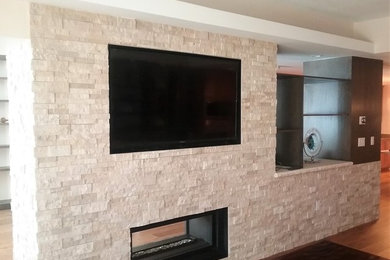 Imagen de salón abierto moderno grande con suelo de madera en tonos medios, chimenea de doble cara, marco de chimenea de piedra, televisor colgado en la pared y suelo marrón
