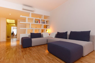 Modelo de salón abierto actual de tamaño medio sin chimenea con paredes blancas, suelo de madera clara y televisor independiente