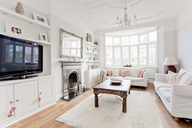ロンドンにある中くらいなヴィクトリアン調のおしゃれな独立型リビング (白い壁、淡色無垢フローリング、標準型暖炉、金属の暖炉まわり、据え置き型テレビ、ベージュの床) の写真