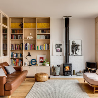 This is an example of a medium sized retro living room in Buckinghamshire with beige walls, a wood burning stove, a brick fireplace surround, a freestanding tv, brown floors and medium hardwood flooring.