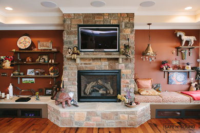 Modelo de salón para visitas abierto clásico de tamaño medio con paredes rojas, suelo de madera clara, todas las chimeneas, marco de chimenea de piedra y televisor colgado en la pared