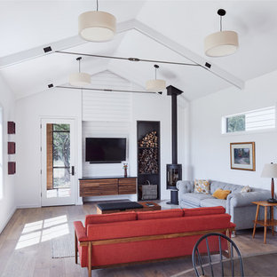 Living room - scandinavian medium tone wood floor and brown floor living room idea in Austin with white walls, a wood stove and a wall-mounted tv