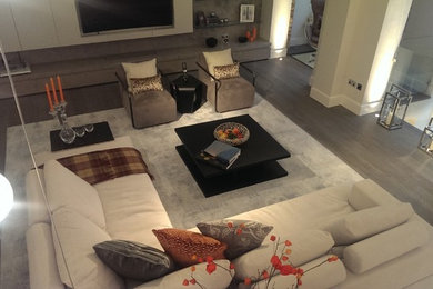 This is an example of a large contemporary formal open plan living room in London with white walls, light hardwood flooring and a built-in media unit.