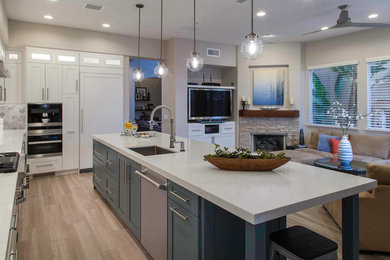 Large traditional u-shaped kitchen/diner in San Diego with a submerged sink, recessed-panel cabinets, white cabinets, engineered stone countertops, grey splashback, glass tiled splashback, stainless steel appliances, light hardwood flooring, an island, beige floors and white worktops.