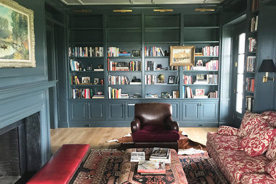 Ejemplo de biblioteca en casa cerrada clásica de tamaño medio con paredes azules, suelo de madera en tonos medios, todas las chimeneas, marco de chimenea de piedra y televisor retractable