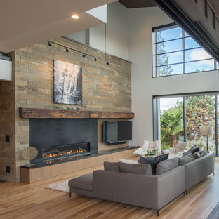Large contemporary open plan living room in Seattle with white walls, medium hardwood flooring, a ribbon fireplace, a wall mounted tv, brown floors, a metal fireplace surround and feature lighting.