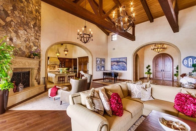 This is an example of an expansive mediterranean open plan living room in San Diego with beige walls, dark hardwood flooring, a standard fireplace, a stone fireplace surround and brown floors.
