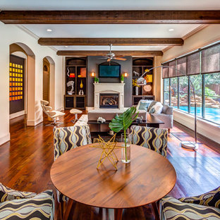 Modelo de salón abierto y arcos, tradicional renovado, grande, con suelo de madera en tonos medios, todas las chimeneas, televisor colgado en la pared y paredes beige