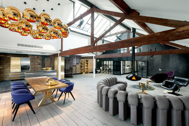Imagen de salón abierto contemporáneo grande con paredes multicolor, suelo de madera clara y chimeneas suspendidas