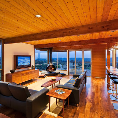 Example of a trendy medium tone wood floor living room design in Santa Barbara with a hanging fireplace and white walls