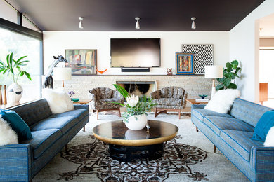 Источник вдохновения для домашнего уюта: гостиная комната в стиле фьюжн с белыми стенами, стандартным камином, фасадом камина из камня, телевизором на стене и синим диваном
