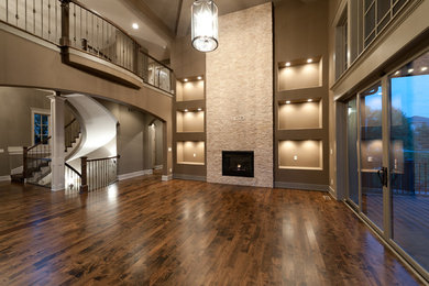 Example of a mid-sized classic open concept medium tone wood floor and brown floor living room design in Kansas City with beige walls, a standard fireplace, a stone fireplace and a wall-mounted tv