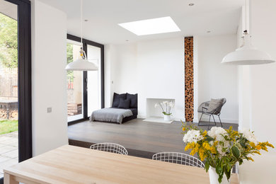Cette photo montre un salon tendance de taille moyenne et ouvert avec un mur blanc, un sol en bois brun, une cheminée standard, un manteau de cheminée en plâtre et aucun téléviseur.