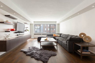 Photo of a modern living room in New York with white walls, medium hardwood flooring, a wall mounted tv and a drop ceiling.